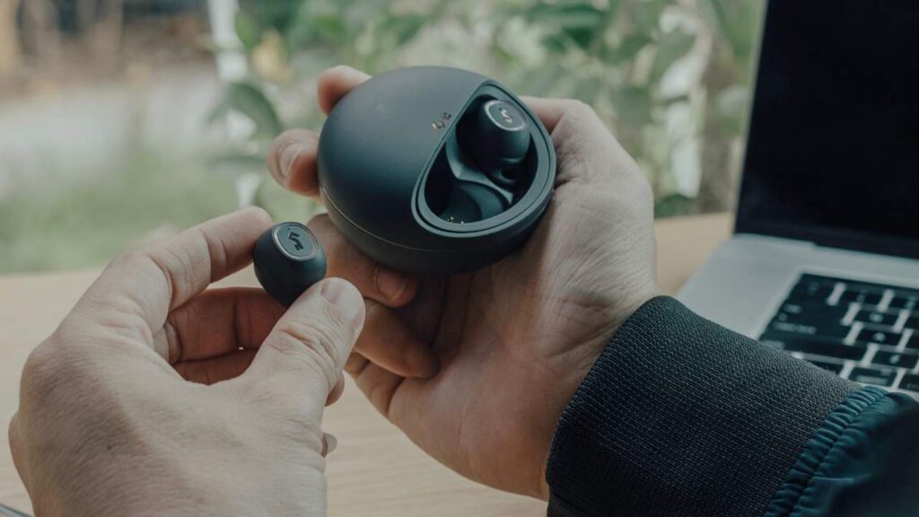 man holding earbuds in round sized case